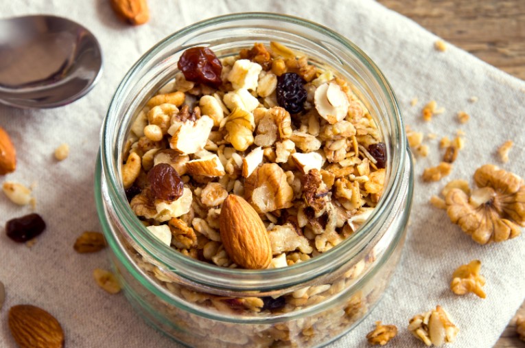 Homemade granola in a glass jar on a white napkin with nuts, oats and a spoon.