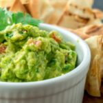 Guacamole in a white dish surrounded by pita chips.