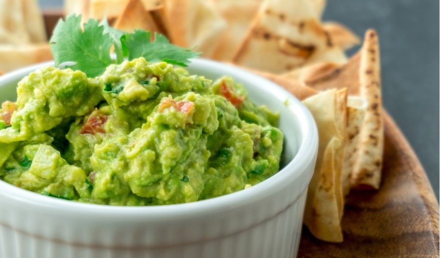 Guacamole in a white dish surrounded by pita chips.
