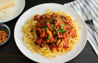 Red lentil bolognese on top of spaghetti noodles on a white plate.