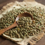 Green lentils on brown cloth on a wooden table with a brown wooden spoon.