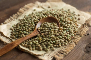 Green lentils on brown cloth on a wooden table with a brown wooden spoon.