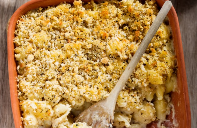 Macaroni and cheese with breadcrumbs in a red backing dish with a wooden spoon.