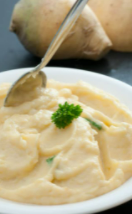 Mashed rutabaga in a white bowl with rutabagas in the background.