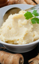 Mashed turnips in a white bowl with a metal spoon topped with green herbs.