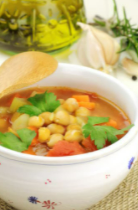 Mediterranean Garbanzo Bean Soup in a white bow with a small floral patter, and a wooden spoon on top.
