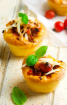 Two mini pizza muffins topped with green herbs and cheese with cherry tomatoes in the background.