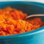 Shredded carrots with spices in a blue bowl.