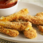 Mozzarella sticks on white plate with white cup of red sauce. Food Styling by Catrine Kelty