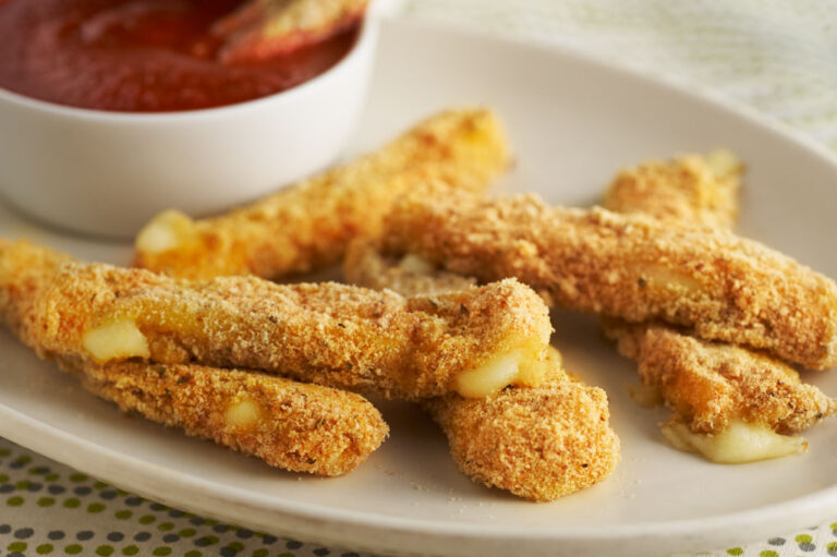 Mozzarella sticks on white plate with white cup of red sauce. Food Styling by Catrine Kelty