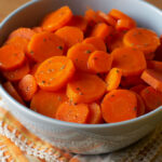 One bowl of sliced orange-glazed carrots on top of a yellow towel.