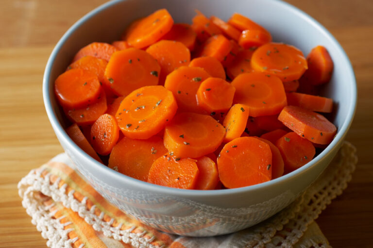 One bowl of sliced orange-glazed carrots on top of a yellow towel.