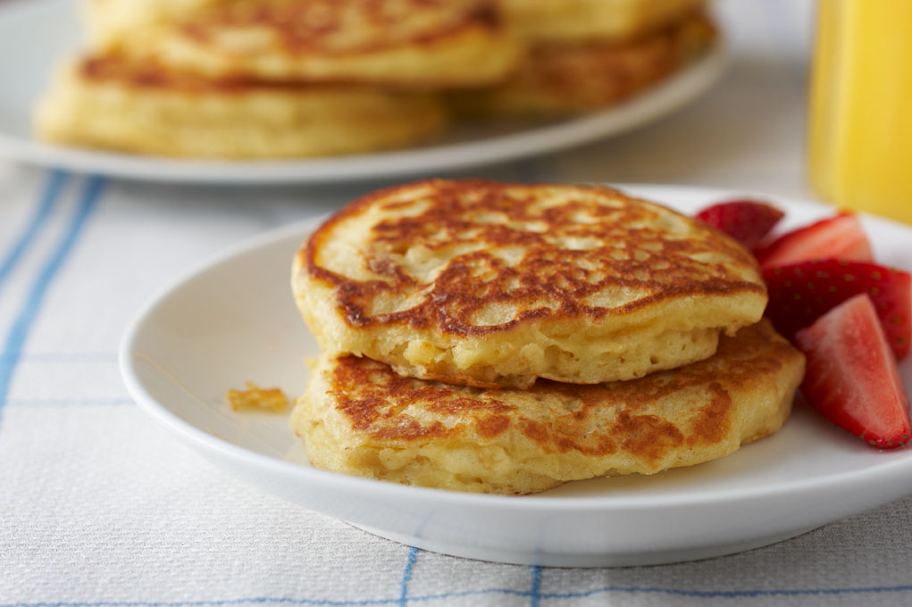 Two orange oatmeal pancakes on a white plate with strawberries.