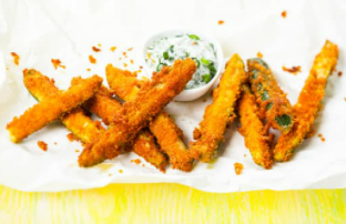 Oven baked zucchini fries on a white platter with dipping sauce.