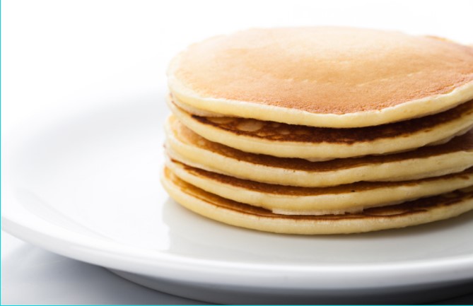 A stack of pancakes on a white plate on top of a white table.