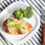 Chicken with cheese and broccoli on a which plate with a striped placemat underneath.
