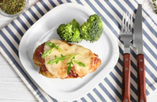 Chicken with cheese and broccoli on a which plate with a striped placemat underneath.