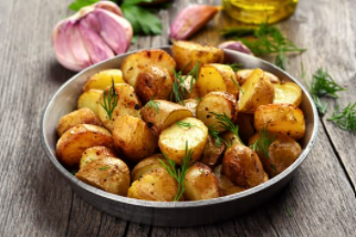 Black bowl with roasted potatoes and green herbs.