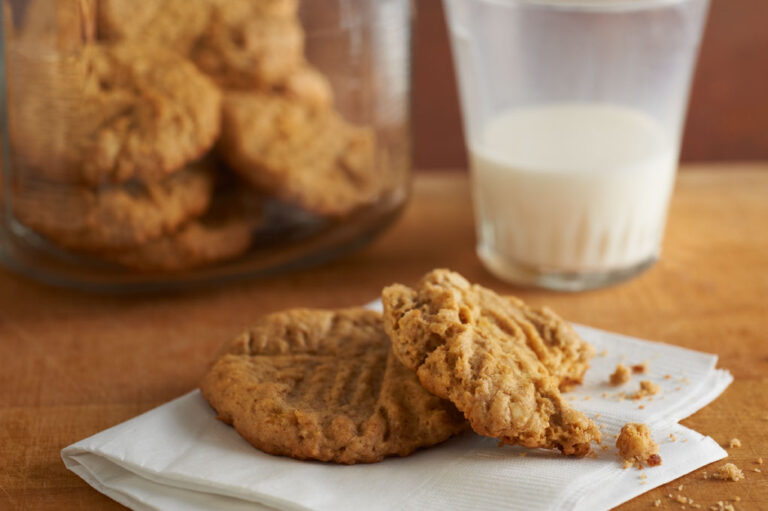 Rolled oat and peanut butter cookies on a white napkin with a jar of cookies and a half full glass of milk in the background