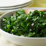 Sauteed greens in a white bowl with a wooden spoon.