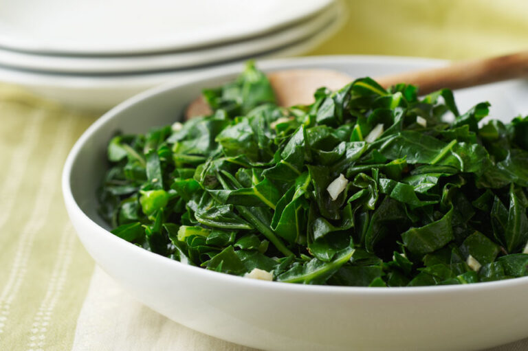 Sauteed greens in a white bowl with a wooden spoon.