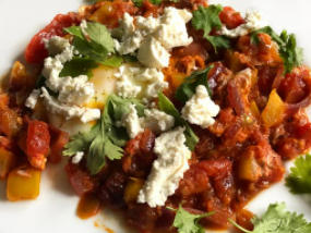 Shakshouka topped with white crumbled cheese and green herbs.