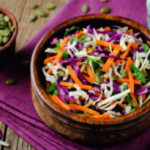 Coleslaw in a wooden bowl with pumpkin seeds in a bowl on the side.
