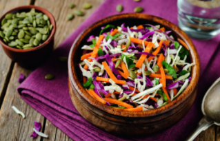 Coleslaw in a wooden bowl with pumpkin seeds in a bowl on the side.