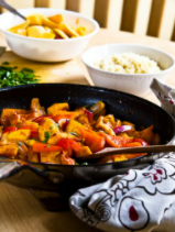 Colorful vegetables and tofu in a black skillet with a wooden spoon.