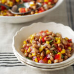 White bowl filled with southwestern black-eyed pea and corn salad with a white serving serving bowl in the background.