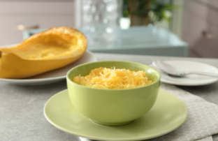 Pale green bowl with spaghetti squash on top of a pale green plate.