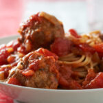 Spaghetti and meatballs in a white bowl.