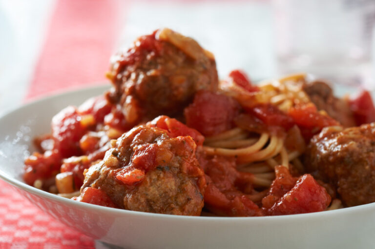 Spaghetti and meatballs in a white bowl.