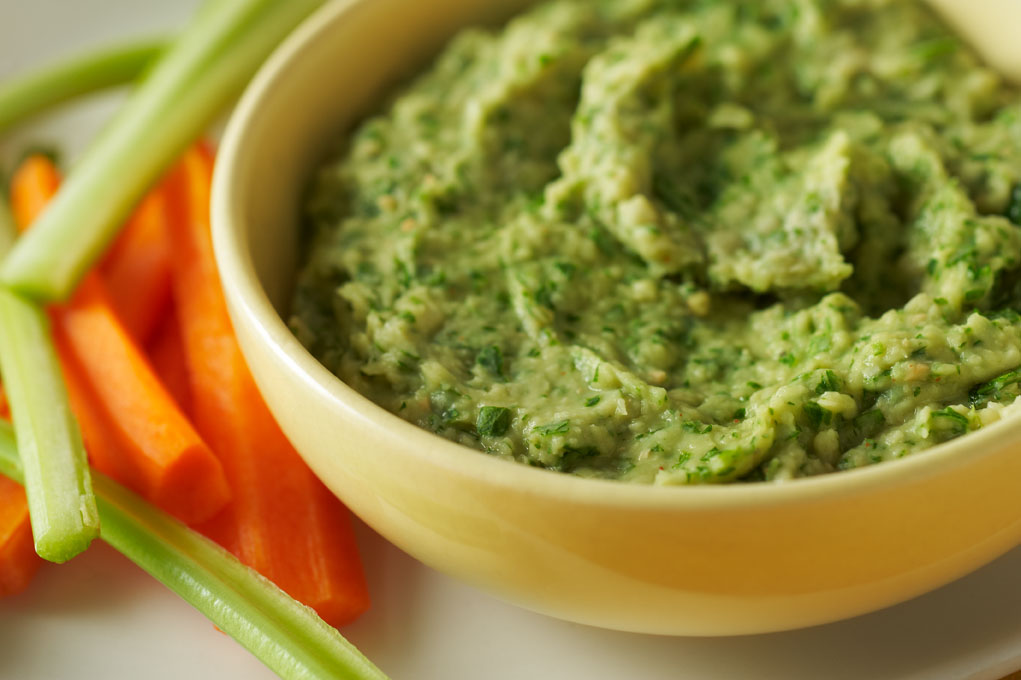 Spicy white bean dip in a yellow bowl with bright orange carrots and lime green celery