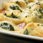 Pasta shells with melted cheese and spinach in a casserole dish.