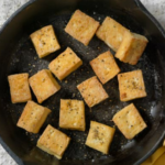 Tofu cooking in a black skillet.