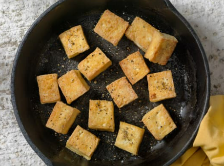 Tofu cooking in a black skillet.