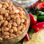 A bowl of pinto beans with an assortment of green and red peppers in the background