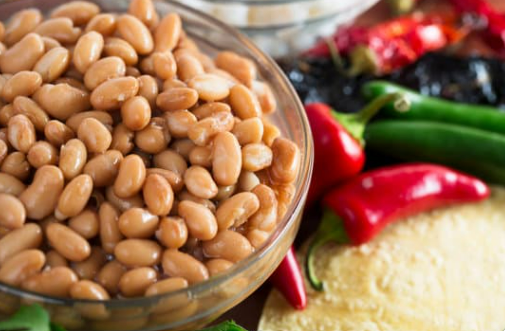A bowl of pinto beans with an assortment of green and red peppers in the background