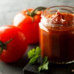 Tomato sauce in a glass jar with fresh tomatoes and herbs on a wooden serving board.