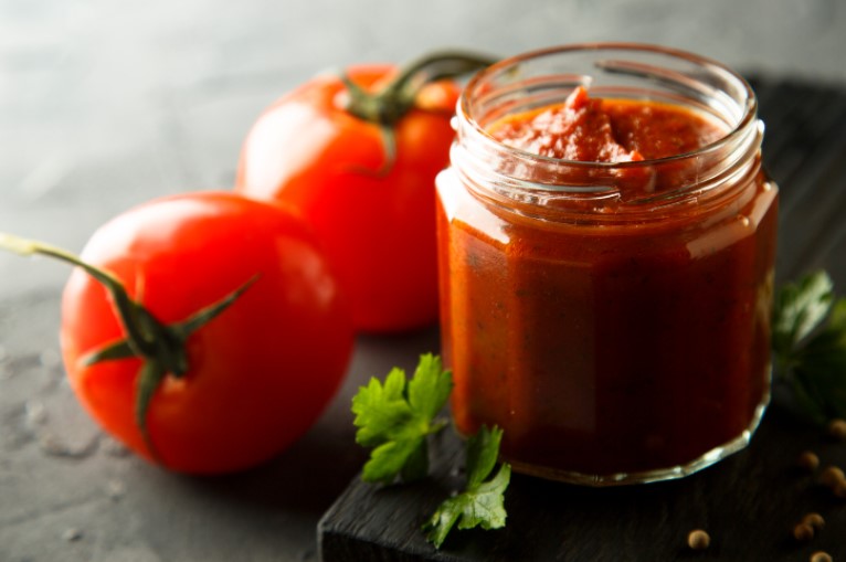 Tomato sauce in a glass jar with fresh tomatoes and herbs on a wooden serving board.