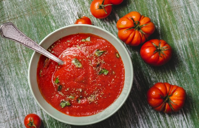 Tomato soup in a white bowl on a green wooden table with fresh tomatoes.