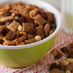 A green bowl full of trail mix sits atop a red and white tea towel