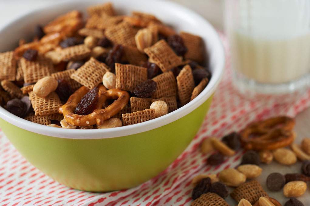 A green bowl full of trail mix sits atop a red and white tea towel