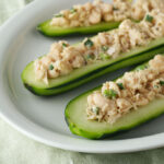 Three halves of cucumbers filled with tuna salad on a white plate.