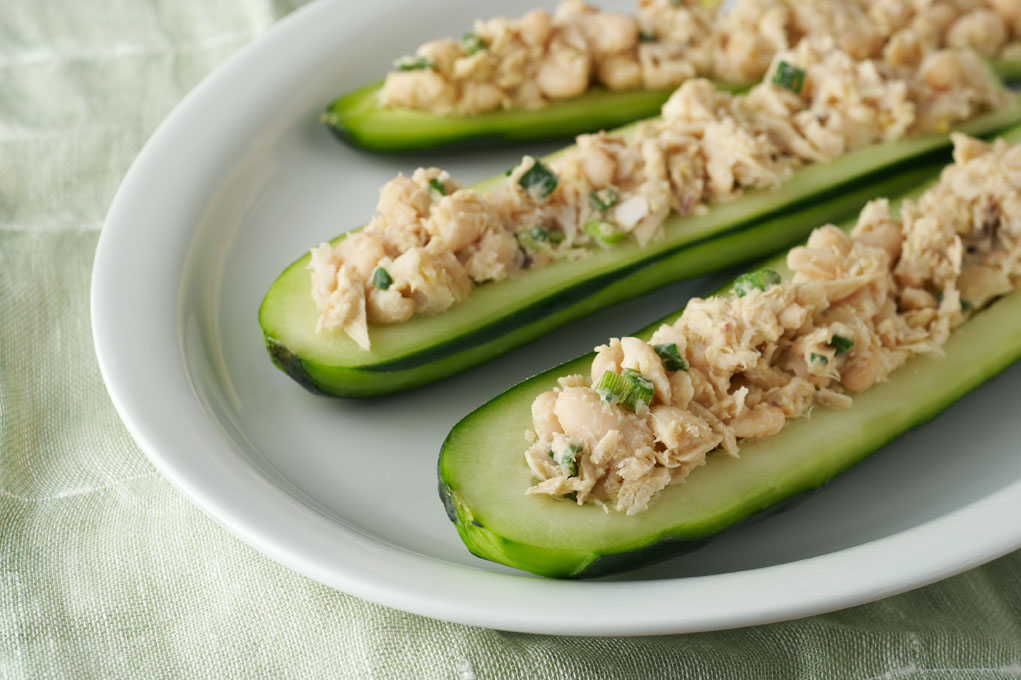 Three halves of cucumbers filled with tuna salad on a white plate.