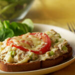 A tuna melt with a side of leafy greens on a white plate