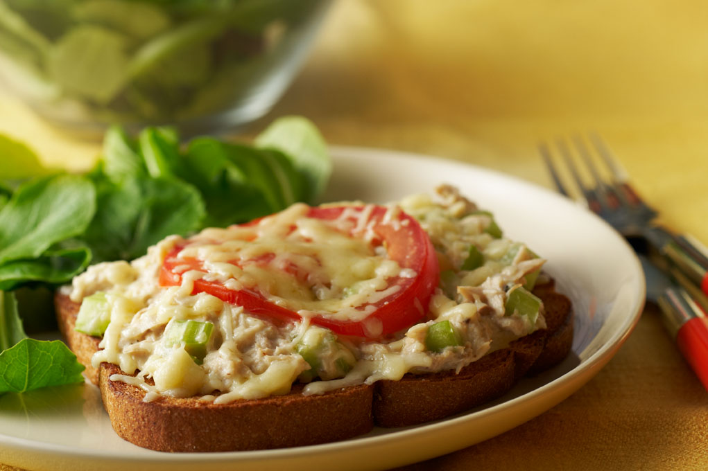 A tuna melt with a side of leafy greens on a white plate