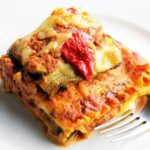 Vegetable lasagna on a white plate with a fork.