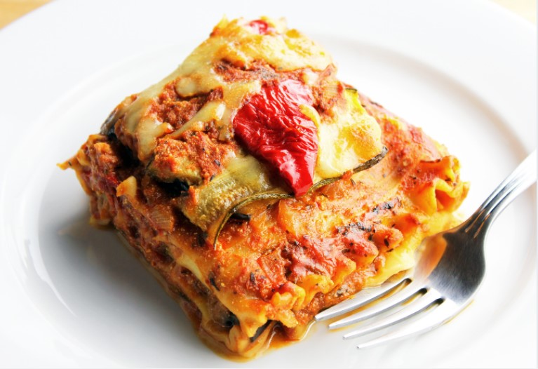 Vegetable lasagna on a white plate with a fork.